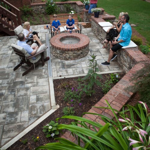 Entertaining family in backyard patio space with concrete pavers, stone/brick fire pit and seat wall