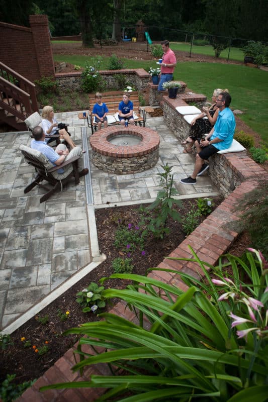 Entertaining family in backyard patio space with concrete pavers, stone/brick fire pit and seat wall