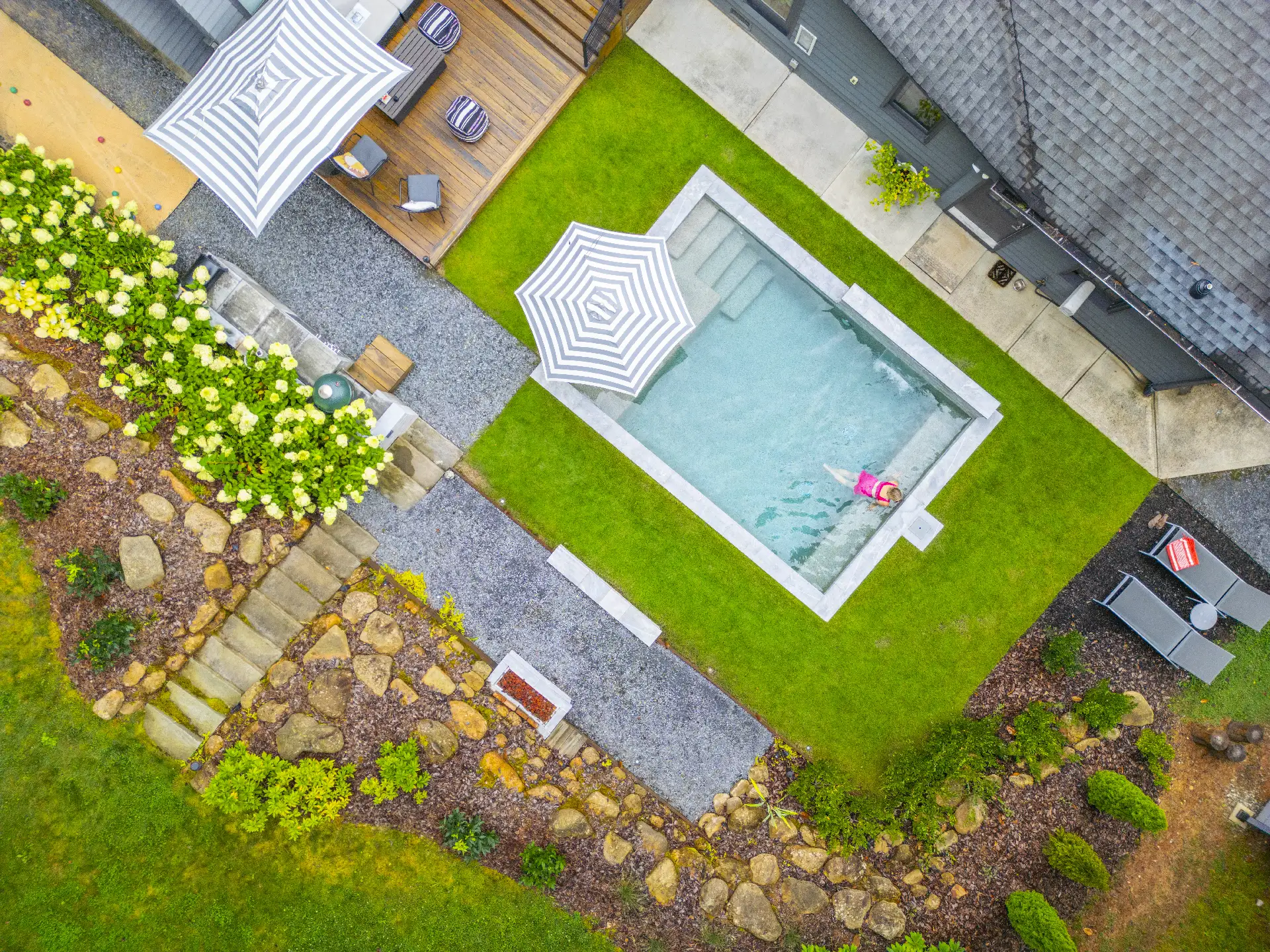 Overhead shot of modern backyard with pool, stone planters, gravel paths, and outdoor seating, surrounded by lush greenery in Atlanta, GA