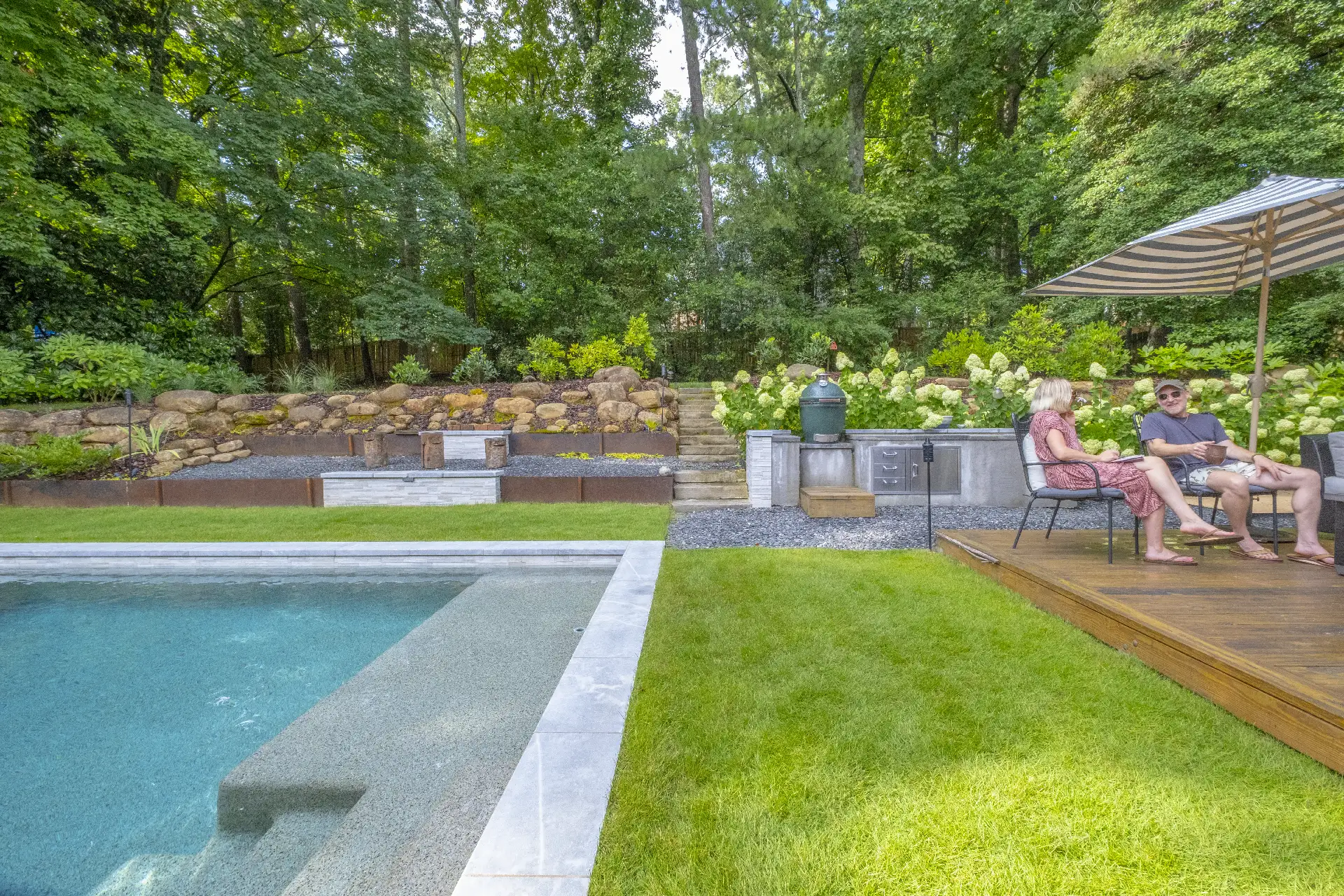 Modern backyard with pool, stone planters, gravel paths, and outdoor seating beside a gray contemporary home, surrounded by lush greenery in Atlanta, GA