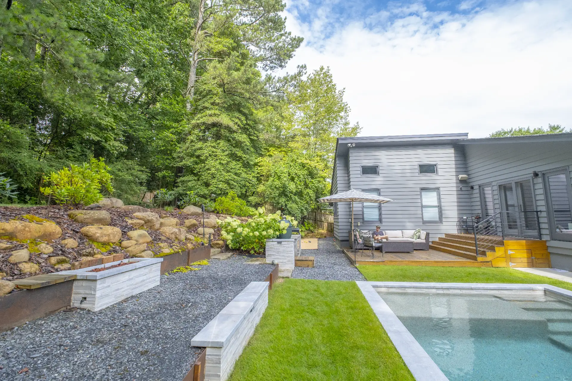 Modern backyard with pool, stone planters, gravel paths, and outdoor seating beside a gray contemporary home, surrounded by lush greenery in Atlanta, GA